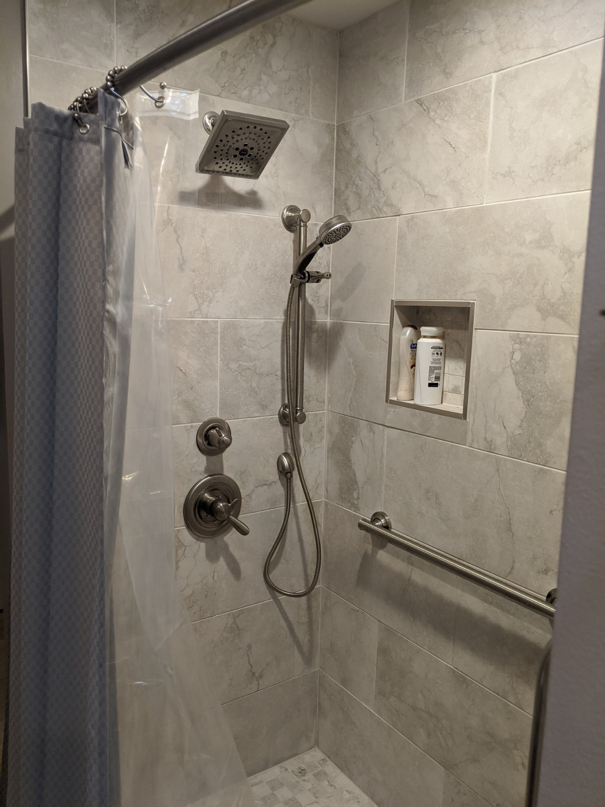 After shower picture, shower has marble style tile in a large format, new grab bars, handheld and shower head