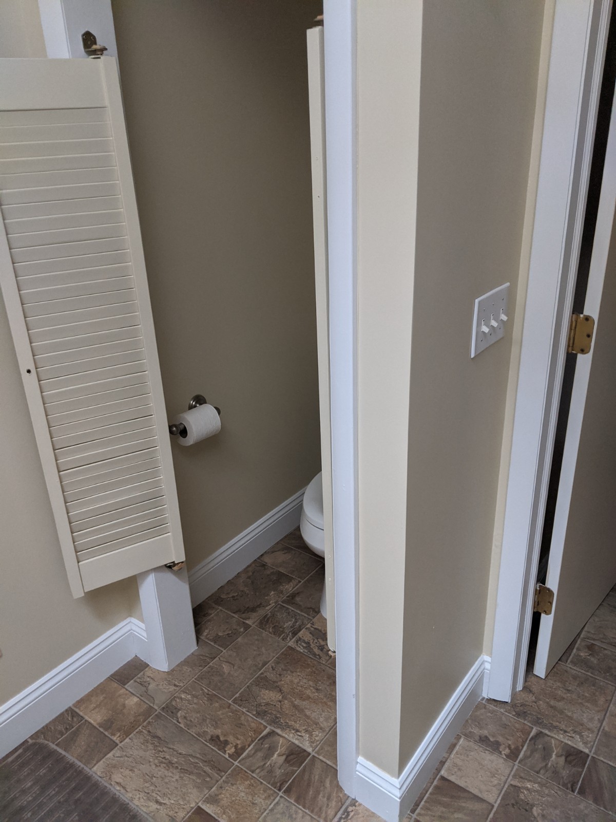 This pictures shows the outdated door on the water closet, as well as the brown 6 x 6 mixed tiles on the linoleum floor.